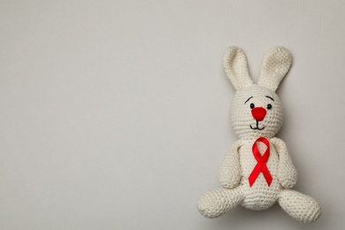 Cute knitted toy bunny with red ribbon on beige background, top view and space for text. AIDS disease awareness