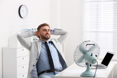 Man enjoying air flow from fan at workplace
