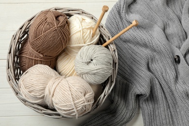Photo of Soft woolen yarns with knitting needles and cardigan on white wooden table, flat lay