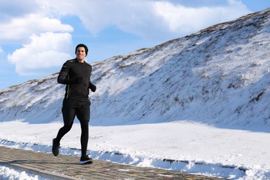 Happy man running past snowy hill in winter. Outdoors sports exercises