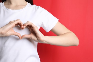 Woman making heart with hands on red background, closeup