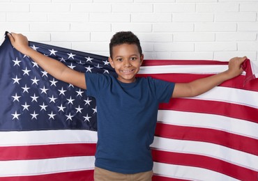 Happy African-American boy holding national flag near white brick wall