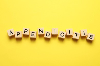 Photo of Word Appendicitis made of wooden cubes with letters on yellow background, top view