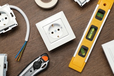 Photo of Set of electrician's tools and power sockets on wooden table, flat lay