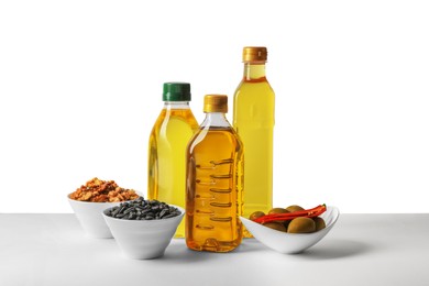 Bottles of different cooking oils, sunflower seeds, walnuts and olives on white background