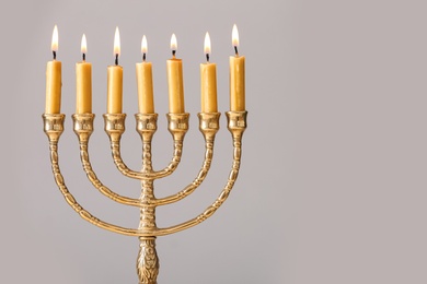 Golden menorah with burning candles on light grey background, space for text