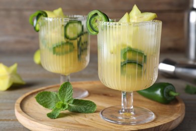 Glasses of spicy cocktail with jalapeno and carambola on wooden table