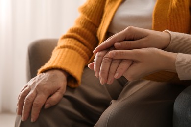 Young and elderly women holding hands together indoors, closeup. Space for text