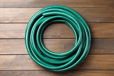 Green garden hose on wooden table, top view