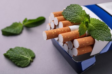 Pack of menthol cigarettes and mint leaves on grey background, closeup