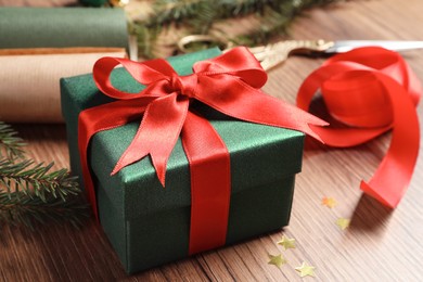 Beautiful Christmas gift box wrapped in paper and decorated with red bow on wooden table, closeup