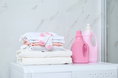 Bottles of detergent and children's clothes on washing machine in bathroom
