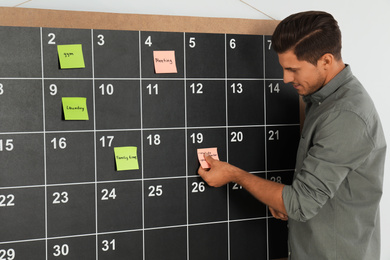 Handsome man putting sticky note on board calendar