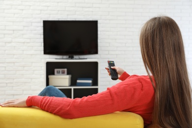 Woman changing TV channel with remote control on sofa in living room. Space for text