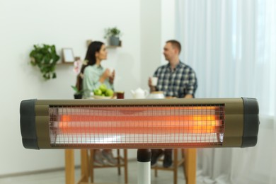 Photo of Couple spending time in room with modern electric infrared heater, focus on appliance