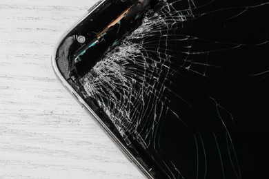 Smartphone with cracked screen on light beige wooden background, closeup. Device repair