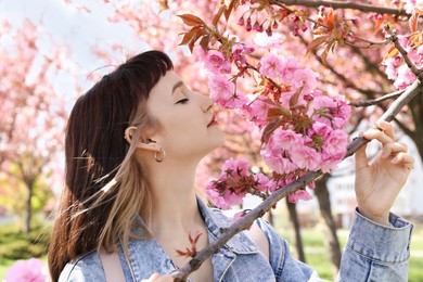 Beautiful young woman near blossoming sakura tree in park