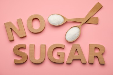 Words No Sugar made of wooden letters and spoons on pink background, flat lay