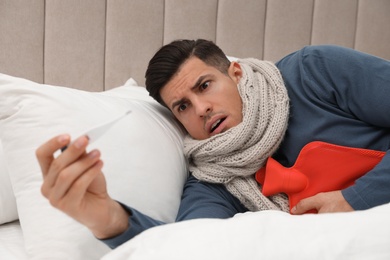 Ill man with hot water bottle checking his temperature at home