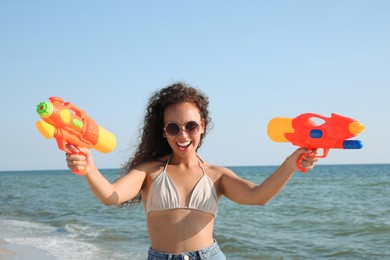African American woman with water guns having fun on beach