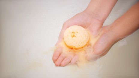 Photo of Woman holding bath bomb over water with foam, above view. Space for text