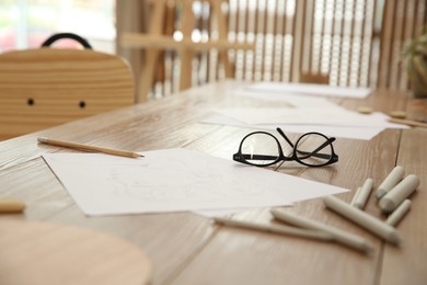 Male portrait drawing, pencils and glasses on wooden table in art studio