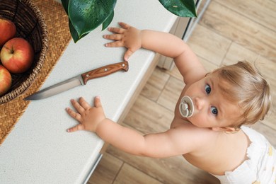 Little child near light countertop with knife, above view. Dangers in kitchen