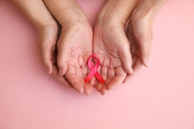 Senior woman and her adult daughter holding pink ribbon on color background, top view. Breast cancer awareness
