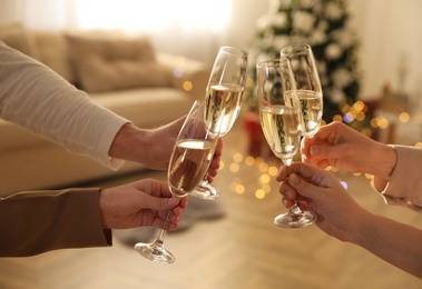 People clinking glasses of champagne in room decorated for Christmas, closeup. Holiday cheer and drink