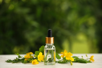 Bottle of natural celandine oil near flowers on white wooden table outdoors