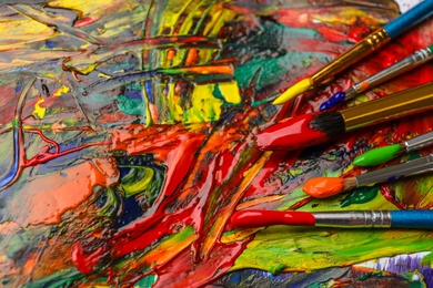 Set of brushes with different paints on artwork, closeup