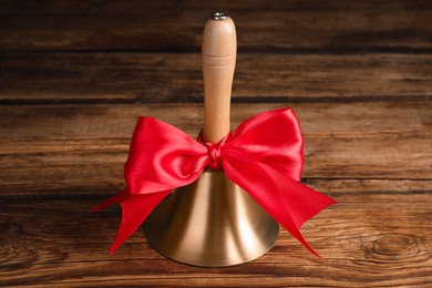 Golden bell with red bow on wooden table. School days