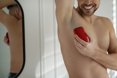 Man applying deodorant in bathroom, closeup. Space for text