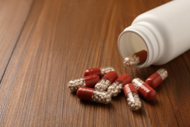 Overturned bottle with dietary supplement capsules on wooden table, closeup. Space for text