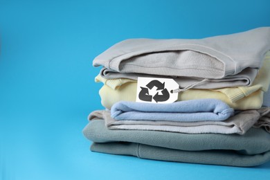 Clothes with recycling label on light blue background, space for text
