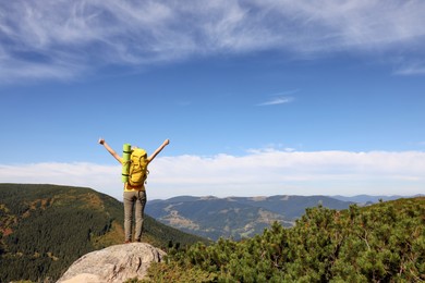 Young woman with backpack on rocky peak in mountains, back view