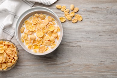 Photo of Tasty cornflakes with milk in bowl on wooden table, flat lay. Space for text