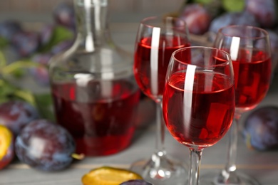 Delicious plum liquor and ripe fruits on table, closeup. Homemade strong alcoholic beverage