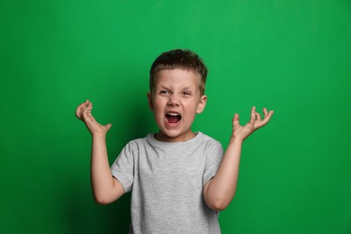 Photo of Angry little boy screaming on green background. Aggressive behavior