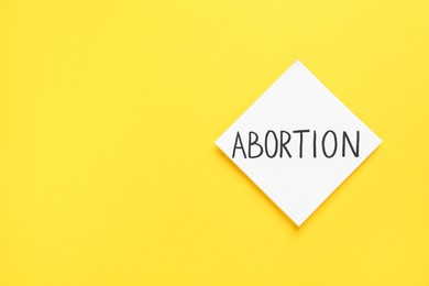 Paper note with word Abortion on yellow background, top view. Space for text