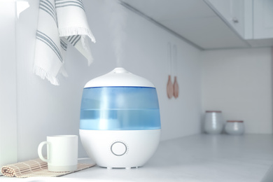 Modern air humidifier, cup and bamboo mat on counter in kitchen. Space for text