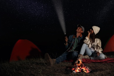 Happy couple with flashlight near bonfire at night. Camping season