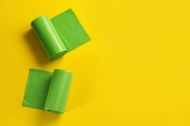 Rolls of green garbage bags on yellow background, flat lay. Space for text