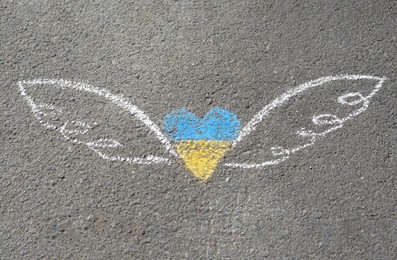 Photo of Heart and wings drawn with blue and yellow chalks on asphalt outdoors, top view