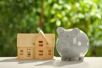 Photo of Piggy bank and house model on wooden table outdoors. Saving money concept