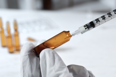 Doctor filling syringe with medication from pharmaceutical ampoule indoors, closeup