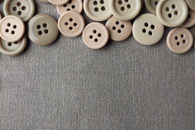 Many plastic sewing buttons on grey fabric, flat lay. Space for text