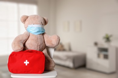 Toy bear with face mask and first aid bag indoors, space for text. Pediatrician practice