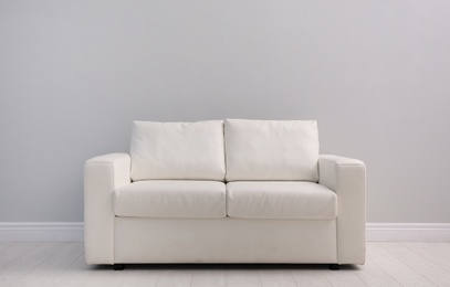 Comfortable white sofa near light wall indoors, space for text. Simple interior
