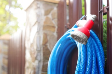 Watering hose with sprinkler hanging on wooden fence in garden, closeup. Space for text